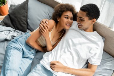 Genç Afro-Amerikan çiftin birbirlerine gülümseyip yatakta kucaklaşmalarını yüksek açıdan izlemek.