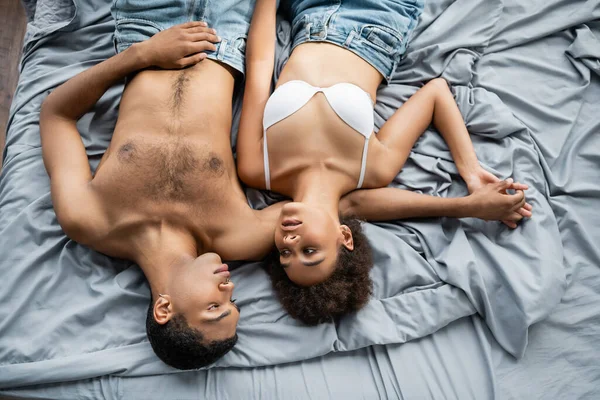 セクシーなアフリカ系アメリカ人の恋人たちが手を取り合ってグレーのベッドの上で — ストック写真
