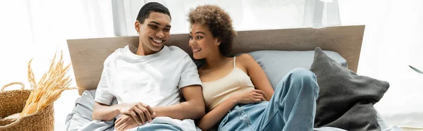 快乐的非洲裔美国女人躺在床上 对着年轻的男朋友笑 挂着横幅 — 图库照片