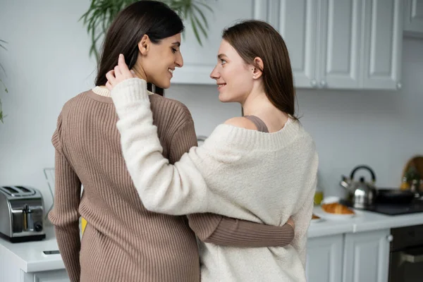 stock image Side view of young lesbian coupe hugging and looking at each other in kitchen 