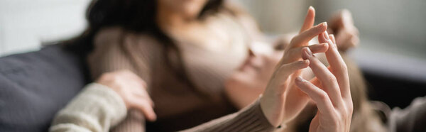 Blurred lesbian couple touching hands while relaxing on couch at home, banner 