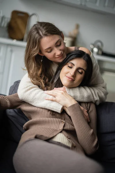Jovem Mulher Suéter Abraçando Sorridente Namorada Sofá — Fotografia de Stock