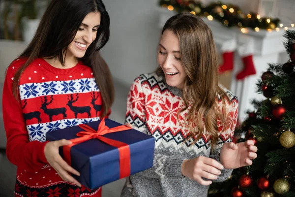 Smiling Woman Giving Present Girlfriend Christmas Tree Home — Stock Photo, Image