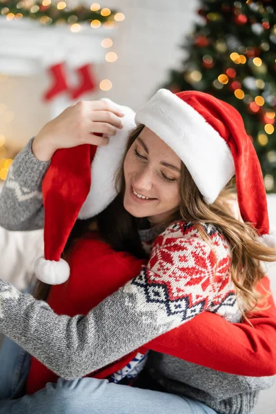 Smiling Woman Santa Hat Embracing Girlfriend New Year Celebration Home — Stock Photo, Image