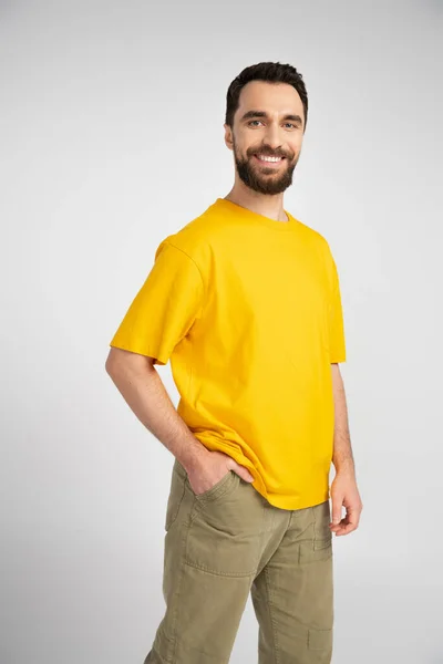 穿着黄色T恤的黑发男子手牵手站在口袋里 对着被灰色隔离的相机笑着 — 图库照片