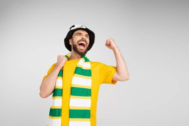Çizgili atkı ve futbol şapkalı neşeli adam çığlık atıyor ve zafer jestini gri renkte gösteriyor.