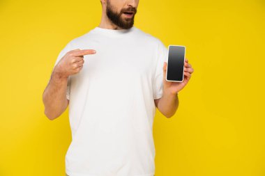 Beyaz tişörtlü sakallı adamın kısmi görüntüsü sarı ekranda boş ekranlı akıllı telefonu gösteriyor.