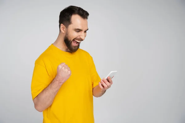 Podekscytowany Brodaty Mężczyzna Smartfonem Pokazując Gest Wygranej Krzyki Izolowane Szarości — Zdjęcie stockowe