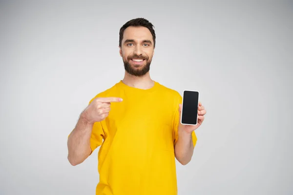 Uśmiechnięty Mężczyzna Żółtej Koszulce Celujący Komórkę Pustym Ekranem Odizolowanym Szaro — Zdjęcie stockowe