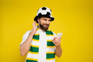 Gözü kapalı futbol fanatiği parmaklarını çapraz tutuyor ve cep telefonunu sarıda izole ediyor.