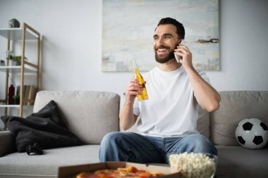 KYIV, UKRAINE - 21 Ekim 2022: neşeli bir adam elinde bira şişesiyle futbol maçından sonra telefonla konuşuyor.