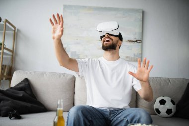 KYIV, UKRAINE - 21 Ekim 2022: oturma odasında vr kulaklık takmış heyecanlı adam
