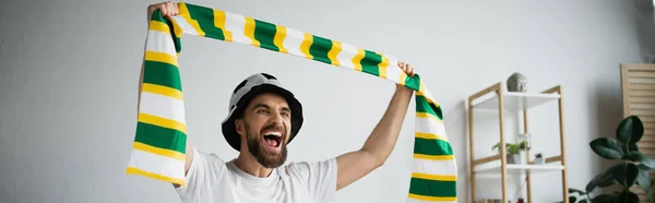 amazed man in hat holding scarf while watching championship, banner