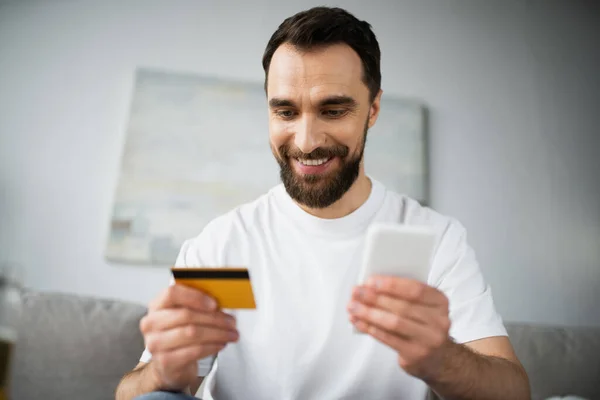 Homem Alegre Segurando Cartão Crédito Usando Smartphone Enquanto Faz Compras — Fotografia de Stock