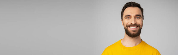 portrait of cheerful bearded man in bright yellow t-shirt looking at camera isolated on grey, banner