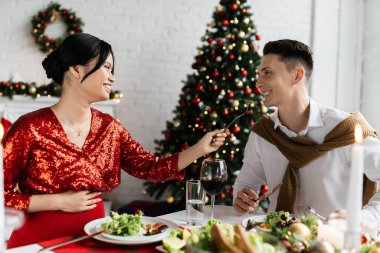 Mutlu ve hamile Asyalı bir kadın romantik bir Noel yemeğinde eğlenirken kocasını besliyor. 