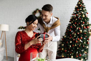 Mutlu ve hamile Asyalı kadın genç kocadan Noel hediyesi alıyor.