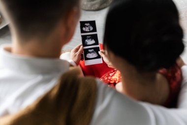 back view of blurred couple holding ultrasound scan with pregnancy confirmation clipart