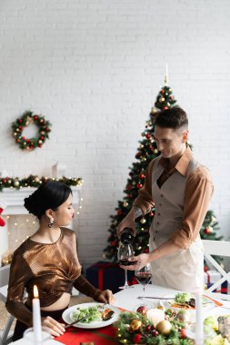Evde romantik bir Noel yemeği sırasında Asyalı bir kadının yanına kırmızı şarap döken zarif bir adam.