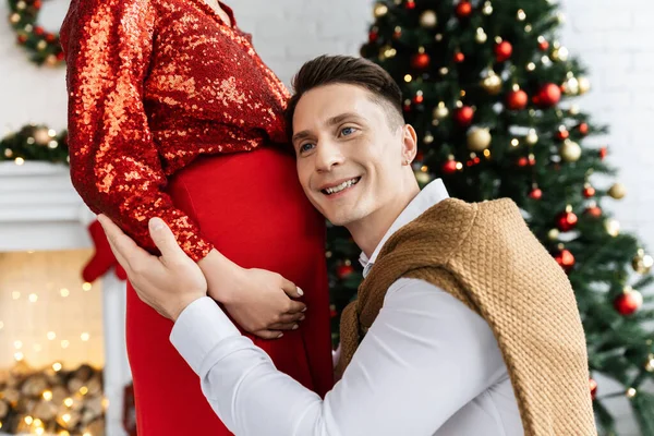 Pleased Man Leaning Tummy Pregnant Wife Red Shiny Blouse Christmas — Stock Photo, Image