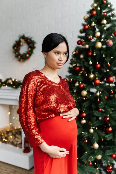 Pregnant Asian Woman Red Shiny Blouse Touching Tummy Looking Away — Stock Photo, Image