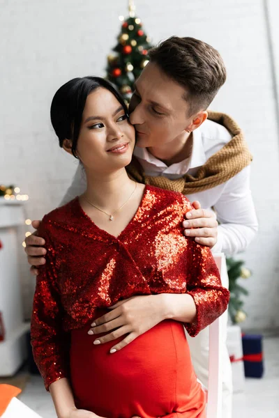 Man Kissing Pregnant Asian Wife Festive Clothes Christmas Celebration — Stock Photo, Image