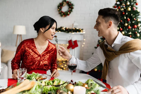 Homem Alegre Alimentando Grávida Elegante Asiático Esposa Durante Natal Ceia — Fotografia de Stock