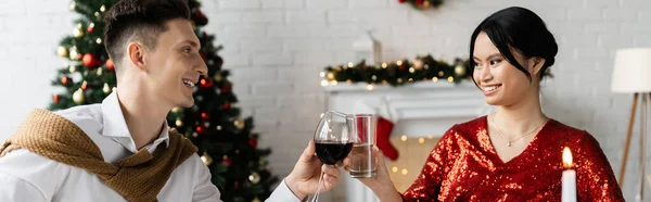 在圣诞庆祝活动中 快乐的跨种族夫妇互相望着对方 同时在酒杯上挂着红旗 — 图库照片