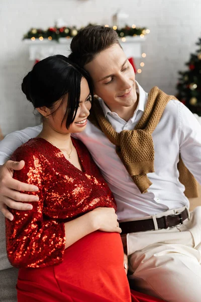 Tevreden Man Omarmen Zwangere Aziatische Vrouw Rood Glanzende Kleren Terwijl — Stockfoto