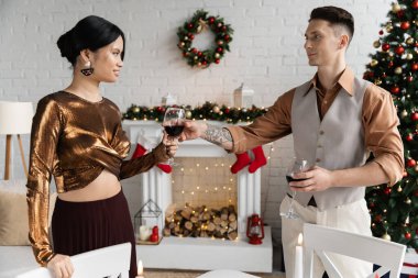 Dövmeli adam, mutlu Asyalı karısına Noel kutlaması sırasında bir bardak şarap veriyor. 