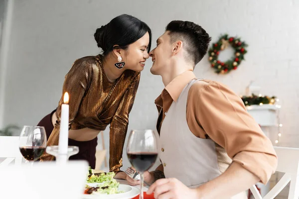 happy interracial couple smiling near festive dinner on dining table during Christmas celebration