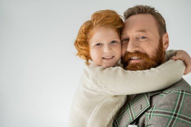 Örgü ören kızıl saçlı olumlu çocuk. Babamı kucaklıyor. Gri renkte izole edilmiş. 