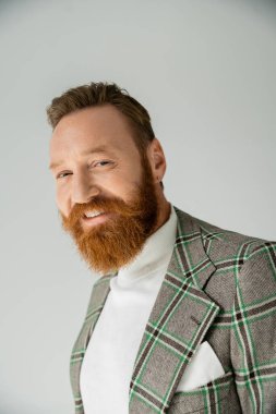 Gri renkli ceketli sakallı adam kameraya gülümsüyor. 