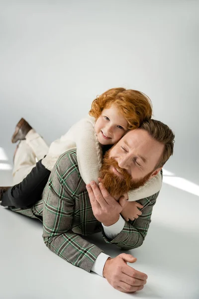Redhead Bambino Maglione Abbracciando Papà Allegro Mentre Sdraiato Sfondo Grigio — Foto Stock
