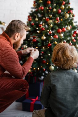 Kızıl saçlı baba ve oğulun evdeki bulanık Noel ağacını dekore edişinin arka görüntüsü