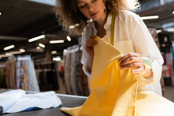 curly salesperson holding yellow fabric while working in textile shop 