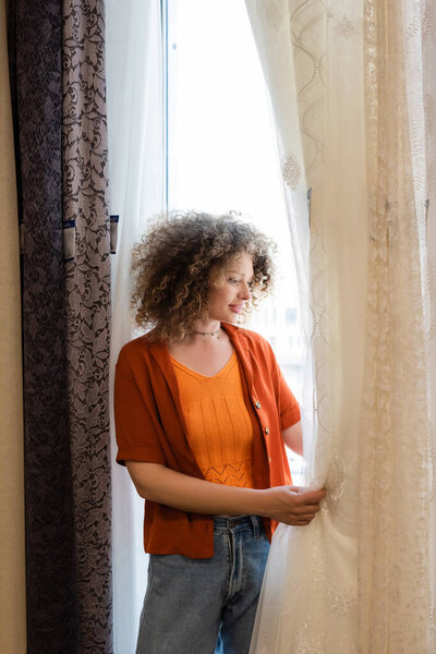 young and curly woman choosing curtains in textile shop