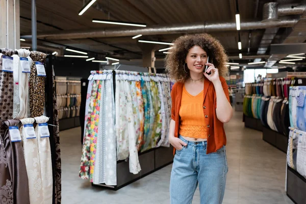 stock image Curly customer talking on mobile phone near cloth samples in textile store 