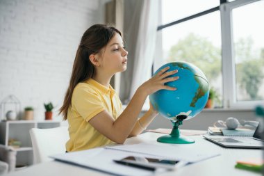 Esmer kız evde coğrafya öğreniyor ve küreye bakıyor.