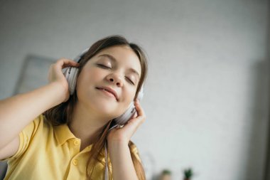 Düşük açılı, kulaklıkla müzik dinleyen, gözleri kapalı, mutlu, reşit olmayan bir kız.