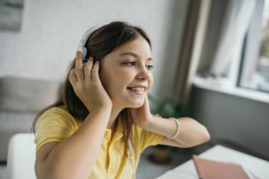 Neşeli kız müzik dinlerken kulaklıklara dokunuyor ve eve bakıyor.