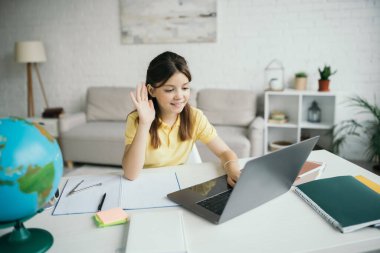 happy girl waving hand during video chat on laptop while learning at home clipart