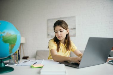 genç kız ödevlerini yaparken dizüstü bilgisayara bakıyor ve daktilo kullanıyor.
