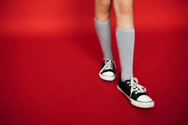 赤の背景に黒と白のガムシューズを着た灰色の膝の靴下の子供の部分的なビュー — ストック写真