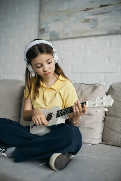 Displeased Girl Headphones Playing Little Hawaiian Guitar While Sitting Couch — Stock Photo, Image