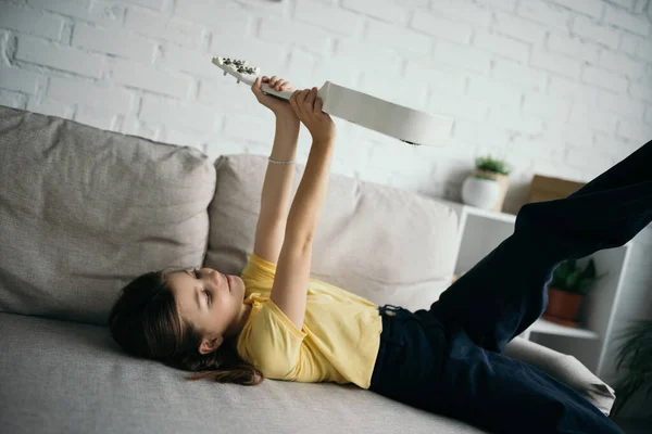 Preteen Girl Lying Couch Living Room Holding Ukulele Raised Hands — Stock Photo, Image
