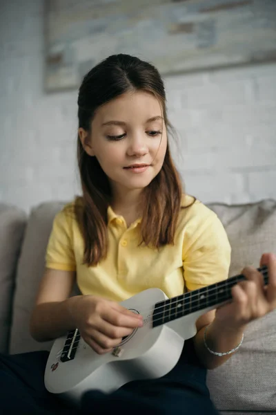 Sorrindo Menina Tocando Pequena Guitarra Havaiana Casa Fundo Borrado — Fotografia de Stock