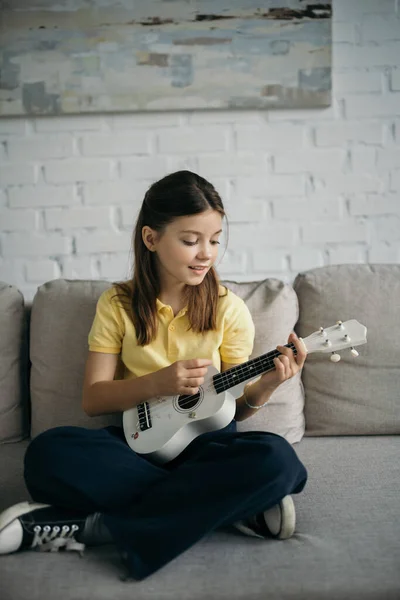 stock image smiling kid playing ukulele while sitting on couch with crossed legs