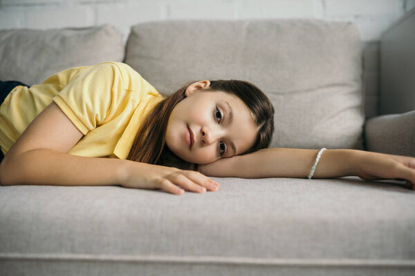 brunette girl in beaded bracelet lying on cozy couch and looking at camera