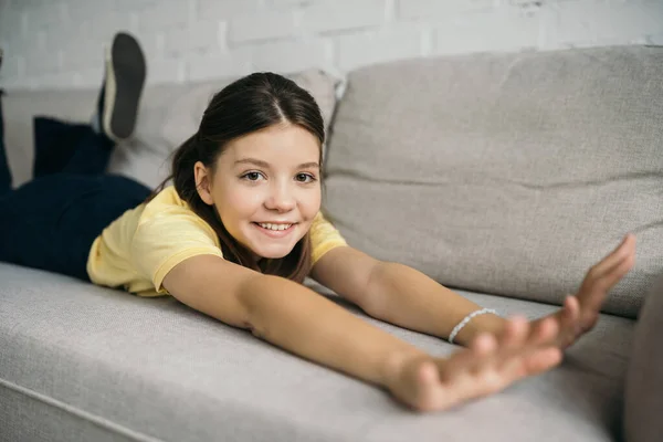 自宅で快適なソファの上でストレッチしながらカメラを見て喜んで女の子 — ストック写真